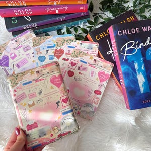 May include: A stack of books with colorful spines, including titles like "Saving" and "Redeeming" by Chloe Walsh. Several decorative cases with a collage of hearts, music notes, and other graphics are also visible.