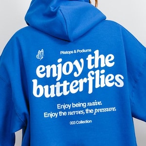 May include: A royal blue hoodie with a hood and long sleeves. The back of the hoodie features white text that reads "enjoy the butterflies" with additional text below. The hoodie is part of the "003 Collection".