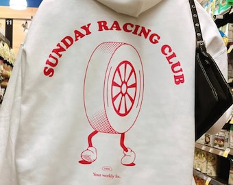 Puede incluir: Sudadera blanca con un gráfico rojo de un neumático con piernas y el texto "SUNDAY RACING CLUB" y "Your weekly fix."