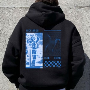 May include: Black hooded sweatshirt with a blue graphic print featuring a racing driver, a chequered flag, and the text "RICCIARDO HONEY BADGER PERTH AUSTRALIA".