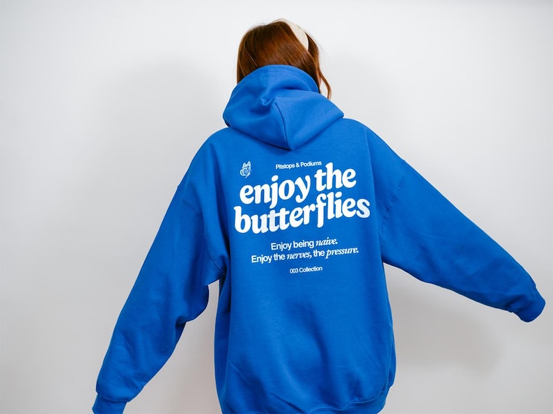 May include: A royal blue hoodie with a hood and long sleeves. The back of the hoodie features white text that reads "enjoy the butterflies" with additional text below. The hoodie is part of the "003 Collection".