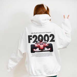 May include: White hooded sweatshirt with a red race car graphic and the text "2002 World Constructors Champion F2002" printed on the back.
