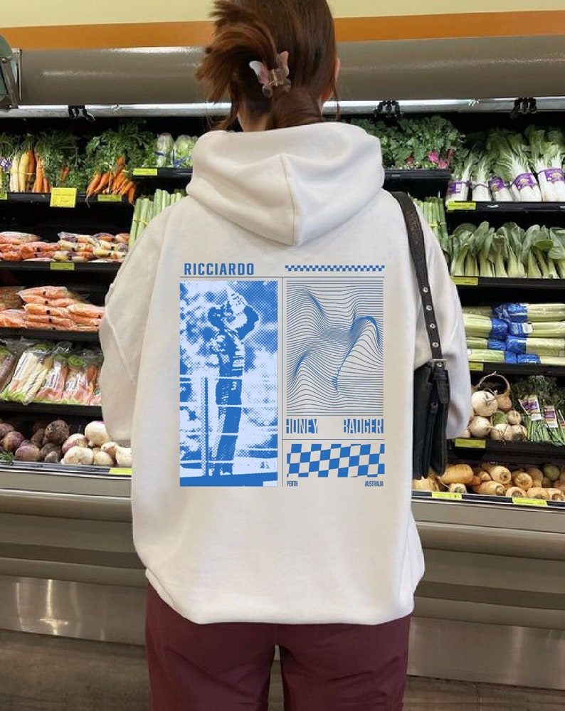 May include: White hooded sweatshirt with a blue graphic print of a race car driver and a chequered flag. The text "RICCIARDO" is printed on the top of the graphic. The text "HONEY BADGER" is printed below the graphic. The text "PERTH AUSTRALIA" is printed below the chequered flag.
