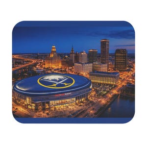 May include: A mousepad featuring a nighttime aerial view of a city skyline with a large stadium in the foreground. The stadium has a blue roof with a yellow logo. The city lights are illuminated against a dark blue sky.