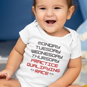 Könnte beinhalten: Ein weißer Baby-Strampler mit dem Text "Montag, Dienstag, Mittwoch, Donnerstag, Training, Qualifikation, Rennen" mit einem karierten Flaggen-Motiv auf beiden Seiten des Wortes "Rennen".