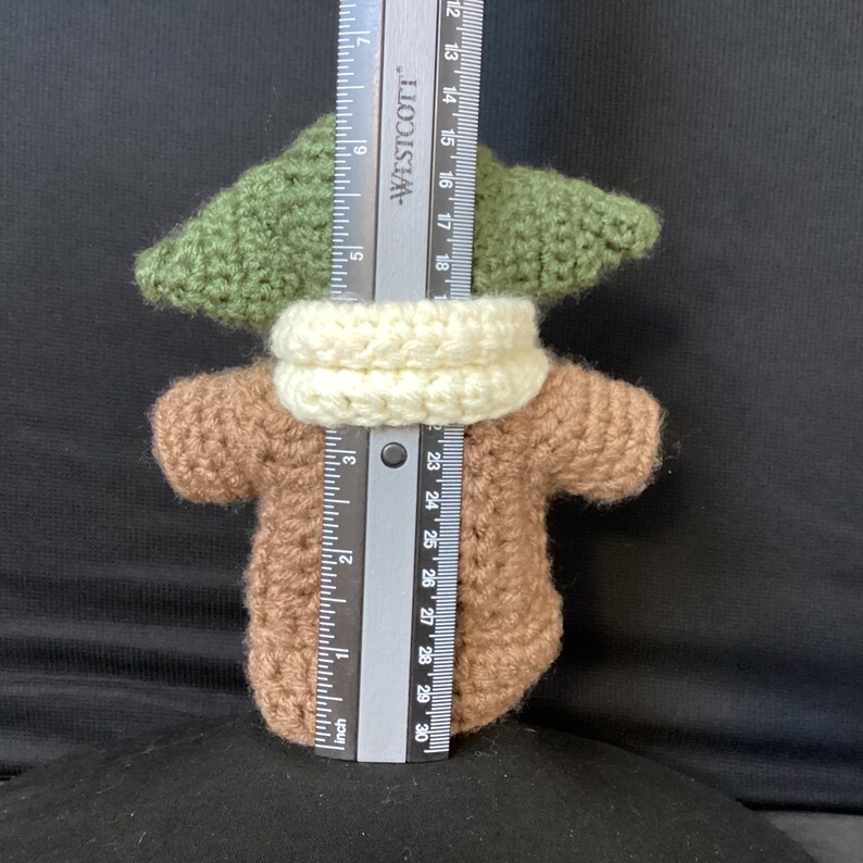 May include: A crocheted green, brown, and white plush toy resembling a character from the Star Wars franchise. The toy is approximately 7 inches tall.
