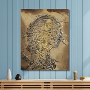 May include: Abstract painting of a face with a swirling, textured design in shades of gold and brown. The painting is framed and hanging on a light blue wall.