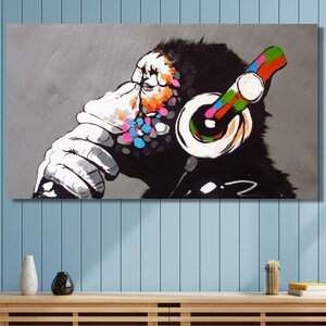 Könnte beinhalten: Ein rechteckiger Wandkunstdruck, der einen stilisierten schwarz-weißen Schimpansen mit großen Kopfhörern zeigt. Das Kunstwerk enthält lebendige Spritzer aus bunten Farbpunkten um das Gesicht und auf den Kopfhörern vor einem grauen Hintergrund.