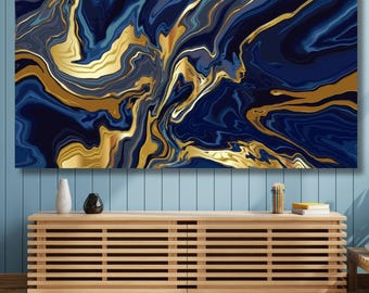 Op de afbeelding: Een rechthoekig wandkunstwerk met een vloeiend marmerpatroon met wervelende diep marineblauwe, lichtblauwe en metallic gouden kleuren. Het kunstwerk is horizontaal opgehangen aan een lichtblauwe wand met panelen boven een houten mediameubel.