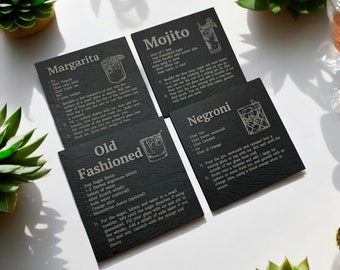 May include: Four black slate coasters with engraved cocktail recipes: Margarita, Old Fashioned, Mojito, and Negroni. Each coaster features a simple line drawing of the cocktail.