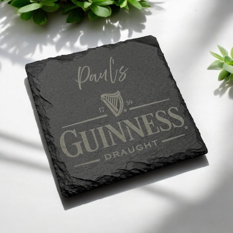 Peut inclure: Sous-verre en ardoise noire avec une inscription blanche qui dit "Paul's" et un logo Guinness gris avec le texte "17 59 GUINNESS DRAUGHT".