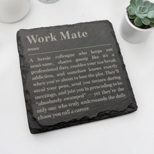 Könnte beinhalten: Ein quadratischer Untersetzer aus schwarzem Schiefer mit einer weiß gravierten wörterbuchartigen Definition des Substantivs Work Mate. Der Text beschreibt eine Person, die Klatsch teilt, Teepausen ermöglicht, Stifte stiehlt und das tägliche Chaos versteht.