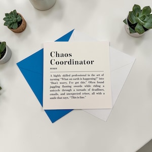 May include: A white card with the words "Chaos Coordinator" in black, on a blue envelope. The card features a definition and description. Two small potted succulents are visible in the background.