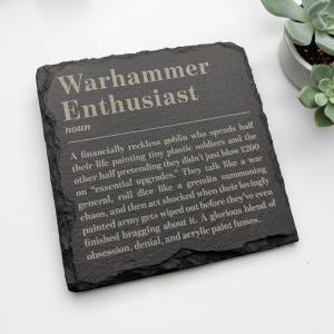 May include: A square black slate coaster featuring the engraved text: Warhammer Enthusiast, noun. A financially reckless goblin who spends half their life painting tiny plastic soldiers and the other half pretending they didn't just blow £200 on essential upgrades.