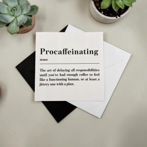 May include: A white card with the word "Procaffeinating" printed in black, along with a definition. The card is on top of a white envelope and a black envelope. Small potted succulents are in the background.