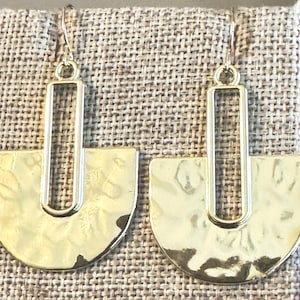 May include: A pair of gold-colored earrings with a hammered texture. Each earring features a rectangular top connected to a semi-circular bottom. The earrings hang from a simple hook.