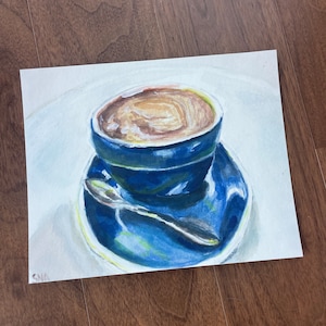 Pu&ograve; includere: Un dipinto ad acquerello di una tazza di caff&egrave; blu con una bevanda al caff&egrave; marrone al suo interno. La tazza &egrave; appoggiata su un piattino blu con un cucchiaio d'argento.