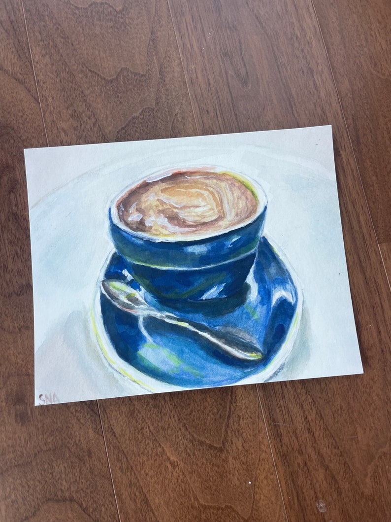 Pu&ograve; includere: Un dipinto ad acquerello di una tazza di caff&egrave; blu con una bevanda al caff&egrave; marrone all'interno. La tazza &egrave; appoggiata su un piattino blu con un cucchiaio d'argento.