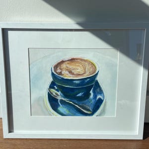 Pu&ograve; includere: Un dipinto incorniciato di una tazza di caff&egrave; blu con una bevanda al caff&egrave; marrone all'interno. La tazza &egrave; su un piattino blu con un cucchiaio d'argento.