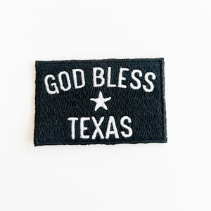 May include: Black fabric patch with white embroidery that reads "God Bless Texas" with a white star in between the words.