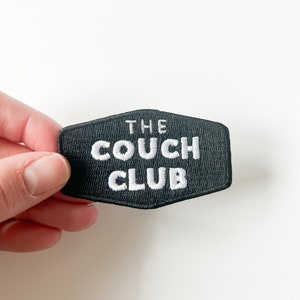 Puede incluir: Parche bordado negro con texto blanco que dice "THE COUCH CLUB".