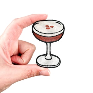 Puede incluir: Un parche bordado para planchar de un cóctel rojo en una copa de martini.