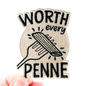 May include: A beige embroidered patch with the words "WORTH every PENNE" in black. The design features a fork holding a piece of penne pasta. The patch has a textured appearance and a white border.
