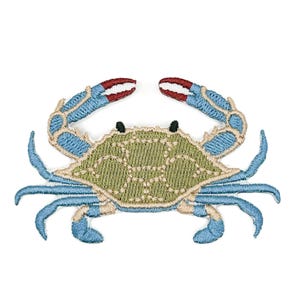 May include: An embroidered iron-on patch shaped like a blue crab. The crab features a textured olive green shell with light tan outlines, bright blue legs and claws, and small black eyes. The tips of the claws are accented with white and red thread.