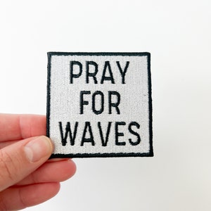 May include: White fabric patch with black embroidered text that reads "Pray for Waves".