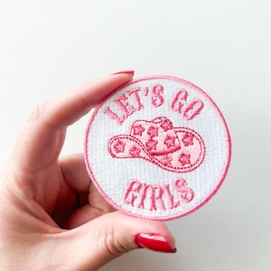May include: Pink and white embroidered patch with a cowboy hat and the text "Let's Go Girls".