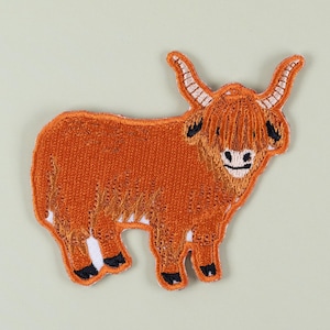 Könnte beinhalten: Gestickter Aufnäher mit einer Highland-Kuh. Der Aufnäher ist überwiegend orange mit braunen und weißen Akzenten und zeigt ein detailliertes Design des zotteligen Fells, der Hörner und Hufe der Kuh. Zum Aufnähen oder Aufbügeln auf Stoff.