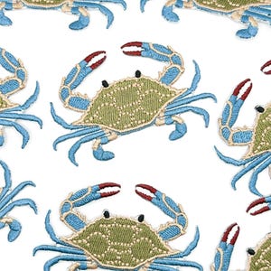 May include: A repeating pattern of embroidered crab patches on a white background. Each crab features a textured olive green shell, bright blue legs and claws, and distinct red tips on the pincers. The embroidery uses visible stitching.
