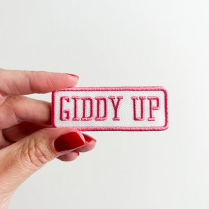 May include: A white patch with pink stitching and the text "Giddy Up" in pink.