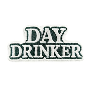 Könnte beinhalten: Ein weißer Aufnäher mit dem Text "DAY DRINKER" in fetten, weißen Buchstaben. Der Text ist dunkelgrün umrandet und hat eine strukturierte, gestickte Optik. Der Aufnäher ist rechteckig und hat ein schlichtes Design.
