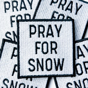 Puede incluir: Cinco parches de tela blanca con texto bordado en negro. Cada parche dice "Pray for Snow".