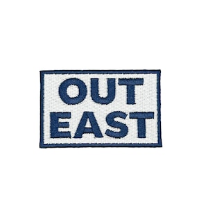May include: Embroidered patch with the words "OUT EAST" in navy blue, centered on a white rectangular background with a navy blue border. The patch is likely for clothing or accessories.