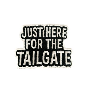 May include: A black and white patch with the text "JUST HERE FOR THE TAILGATE". The text is in a bold, sans-serif font with a white border. The patch is rectangular with rounded corners.