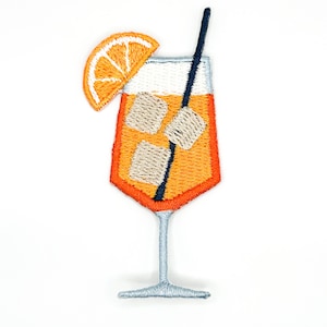 Könnte beinhalten: Ein gestickter Aufnäher in Form eines Cocktailglases, gefüllt mit einer orangefarbenen Flüssigkeit, drei hellen Eiswürfeln und einem dunkelblauen Strohhalm. Eine Orangenscheibe ist am Glasrand befestigt, das einen hellblauen Stiel und Fuß hat.