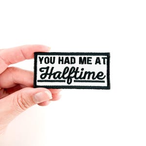 May include: A white patch with black embroidered text that reads "You had me at Halftime".