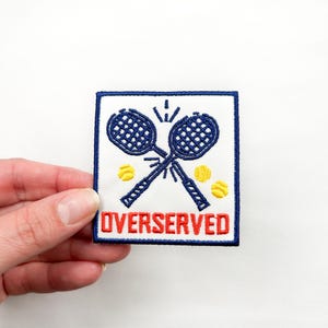 May include: White embroidered patch with a blue tennis racket design and the text "OVERSERVED" in red.