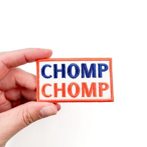 May include: A white patch with an orange border. The patch has the word "CHOMP" written in blue letters on the top line and the word "CHOMP" written in orange letters on the bottom line.