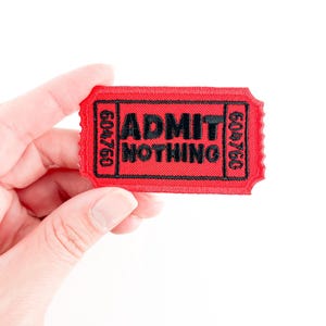 May include: Red fabric ticket patch with black stitching and the text "ADMIT NOTHING" in black.