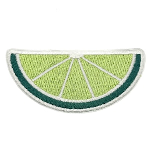 May include: An embroidered patch shaped like a lime wedge. The design features a light green centre with white radial lines representing segments, surrounded by a dark green rind and a thin white border, creating a detailed citrus fruit motif.