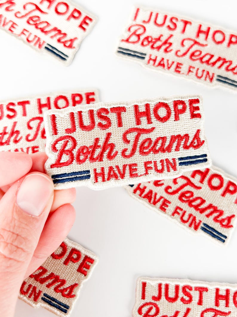 K&ouml;nnte beinhalten: Gestickte Aufn&auml;her mit dem Text "I JUST HOPE Both Teams HAVE FUN" in roter Schrift auf cremefarbenem Hintergrund. Jeder Aufn&auml;her hat zwei blaue Streifen und einen roten Rand. Aufn&auml;her sind auf einer wei&szlig;en Oberfl&auml;che verstreut.