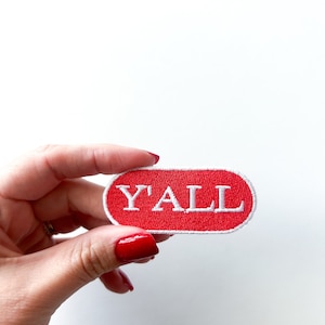 Pode incluir: Patch oval vermelho com texto branco bordado que diz "Y'ALL".