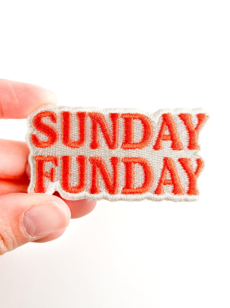 Puede incluir: Parche bordado con las palabras "SUNDAY FUNDAY" en letras de color naranja brillante. El texto est&aacute; cosido sobre un fondo gris claro con un borde blanco. El parche se sostiene sobre un fondo blanco.