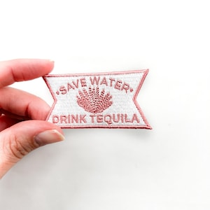 Puede incluir: Un parche blanco para planchar con texto bordado en rosa que dice "Save Water, Drink Tequila".