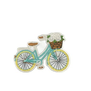 May include: Embroidered patch of a light blue bicycle with yellow wheels and a brown seat. A woven basket on the handlebars is filled with white flowers. The patch has a white border.