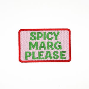 May include: A rectangular patch with a pink background and a red border. The words "SPICY MARG PLEASE" are embroidered in green, centered on the patch. The patch is likely for clothing or accessories.