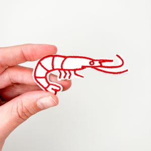 May include: Red embroidered iron-on patch of a shrimp on a white background.